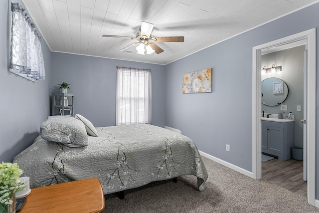 carpeted bedroom featuring ensuite bath, a ceiling fan, baseboards, and ornamental molding