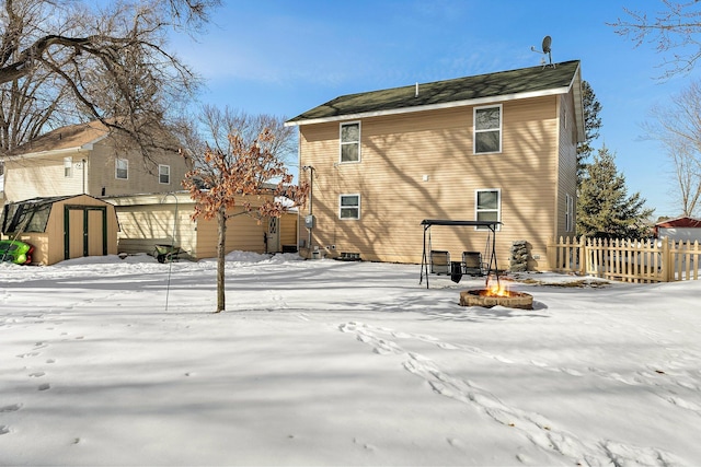 snow covered back of property with fence, a shed, an outdoor fire pit, a garage, and an outdoor structure