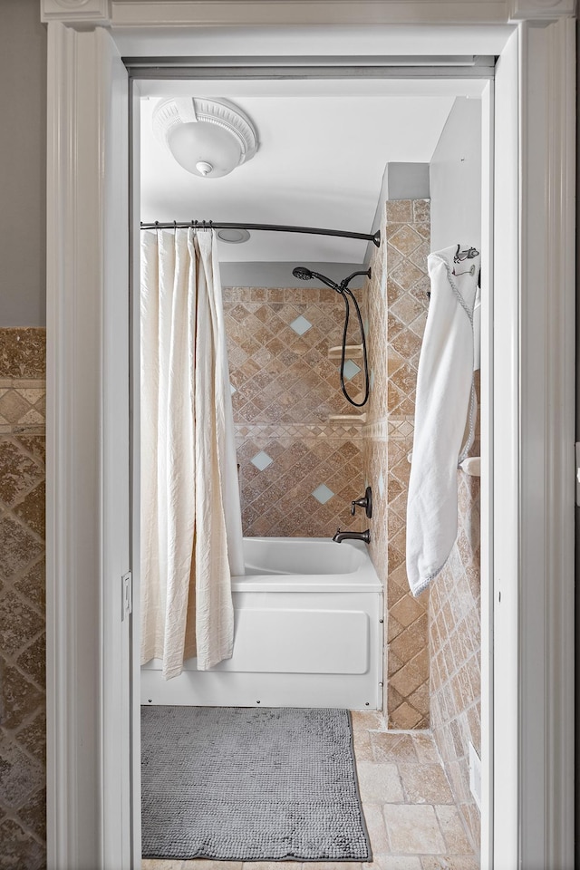 bathroom with tile walls and shower / bath combo with shower curtain