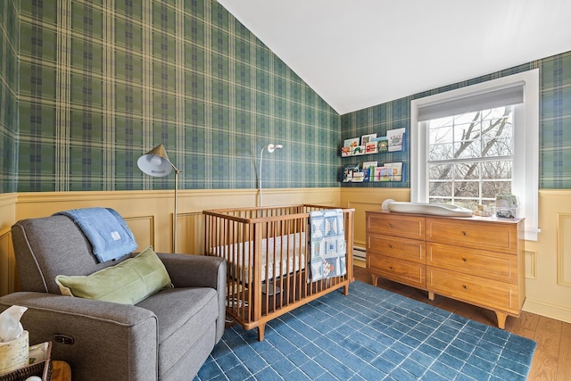 bedroom with dark wood finished floors, wainscoting, wallpapered walls, and lofted ceiling