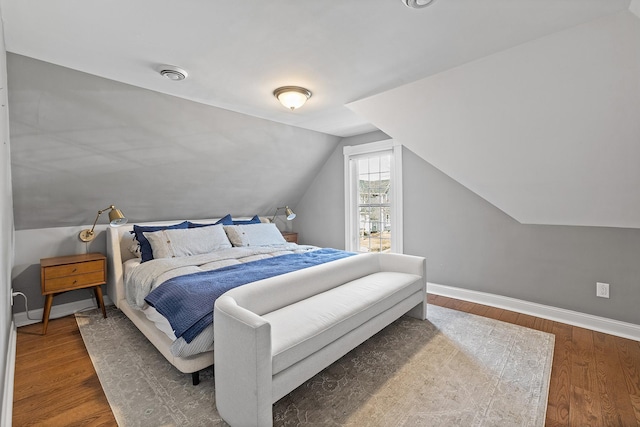 bedroom featuring visible vents, baseboards, lofted ceiling, and wood finished floors