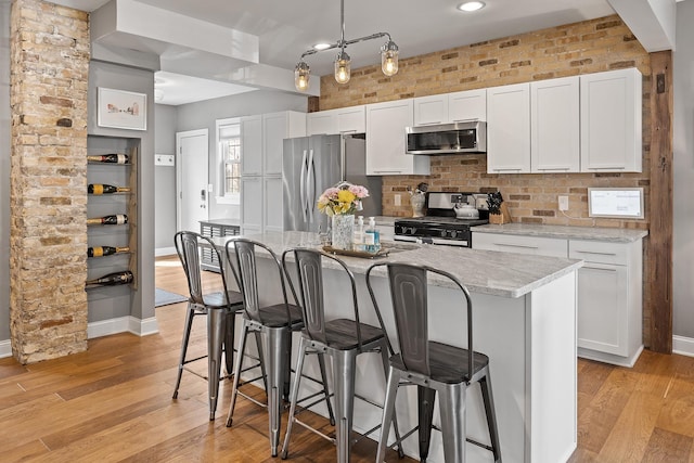 kitchen with white cabinets, brick wall, stainless steel appliances, and light wood-type flooring