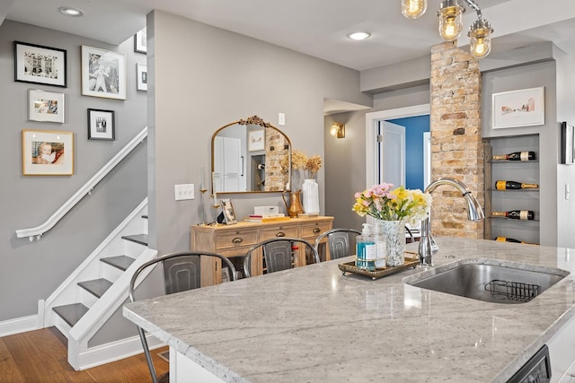 kitchen featuring a sink, light stone counters, wood finished floors, recessed lighting, and baseboards