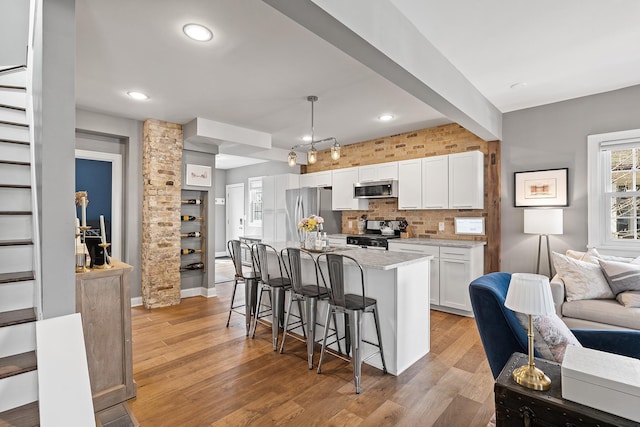 kitchen featuring white cabinetry, light wood-style flooring, decorative backsplash, appliances with stainless steel finishes, and a kitchen bar