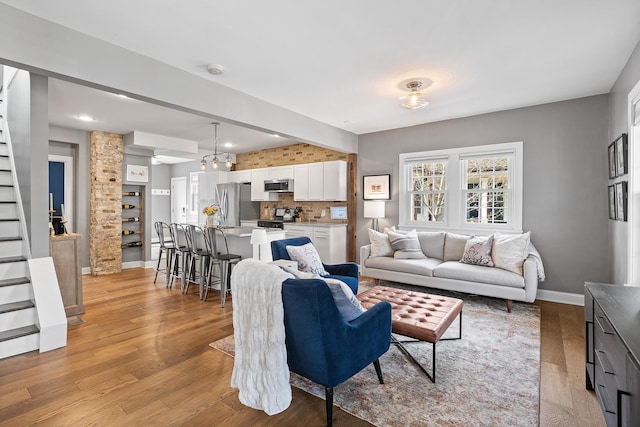 living room featuring stairway, baseboards, and light wood finished floors