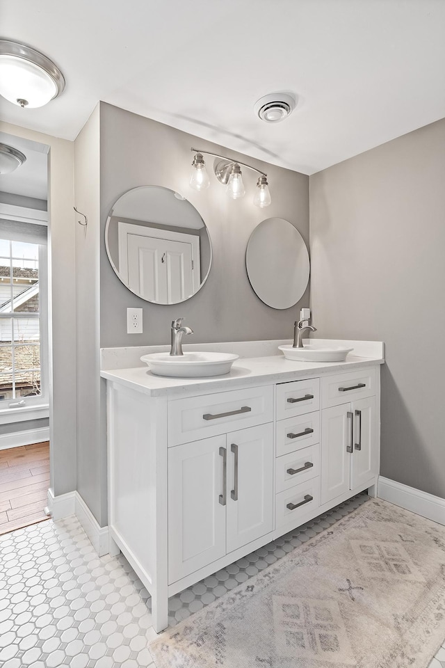 full bath with double vanity, baseboards, visible vents, and a sink