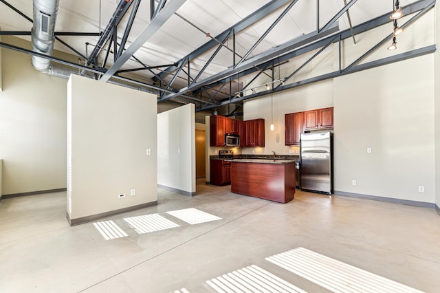 kitchen featuring dark countertops, finished concrete flooring, stainless steel appliances, a high ceiling, and baseboards