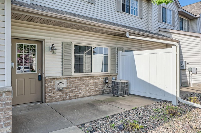 16786 Embers Ave, Lakeville, MN 55024 - property entrance featuring central air condition unit, a shingled roof, brick siding, and a patio area
