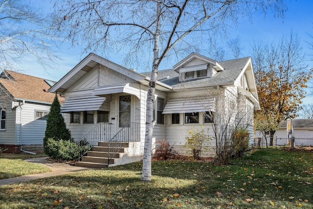 bungalow-style home with a shingled roof, a front lawn, and fence