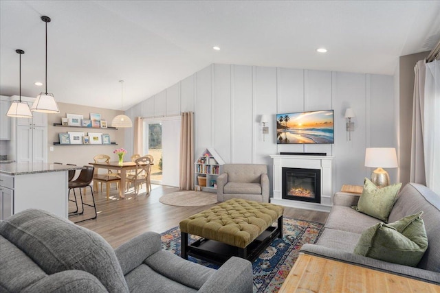 living room featuring a glass covered fireplace, light wood-style floors, and vaulted ceiling