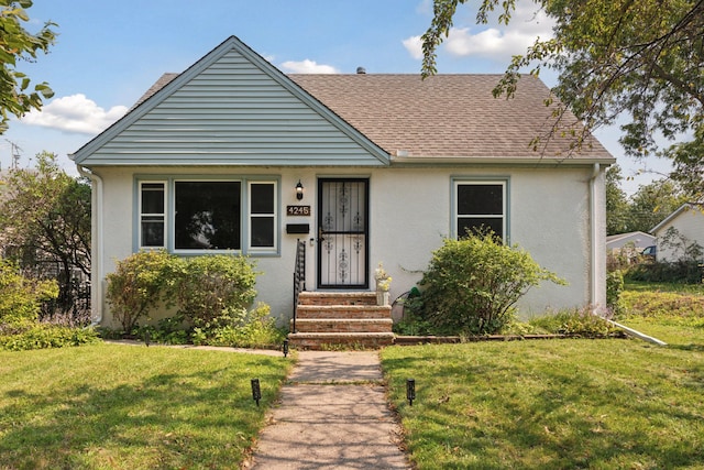 bungalow-style house with a front yard, stucco siding, and a shingled roof