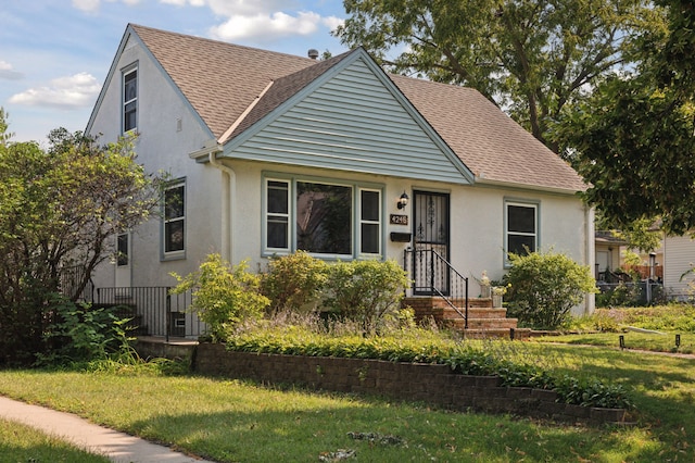 view of front facade with stucco siding, roof with shingles, a front yard, and fence