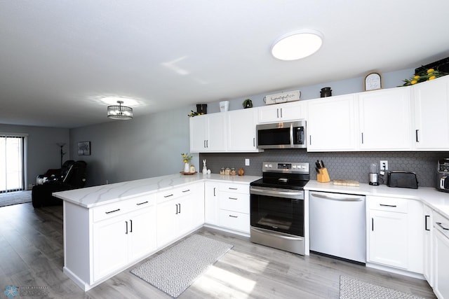 kitchen featuring backsplash, white cabinetry, a peninsula, light wood-style floors, and stainless steel appliances