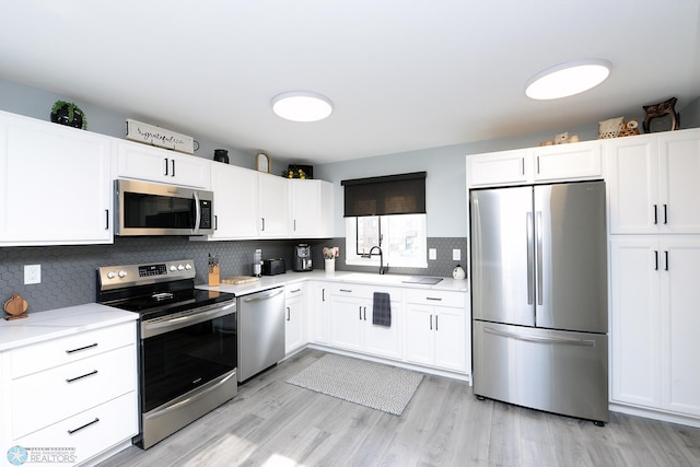 kitchen featuring a sink, tasteful backsplash, white cabinetry, stainless steel appliances, and light countertops