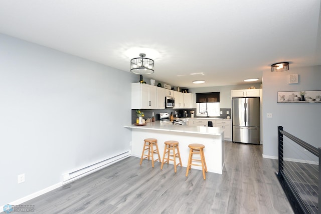 kitchen with tasteful backsplash, a baseboard heating unit, light countertops, appliances with stainless steel finishes, and a peninsula