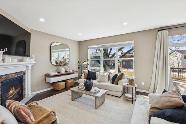 living room featuring recessed lighting, baseboards, a stone fireplace, and wood finished floors