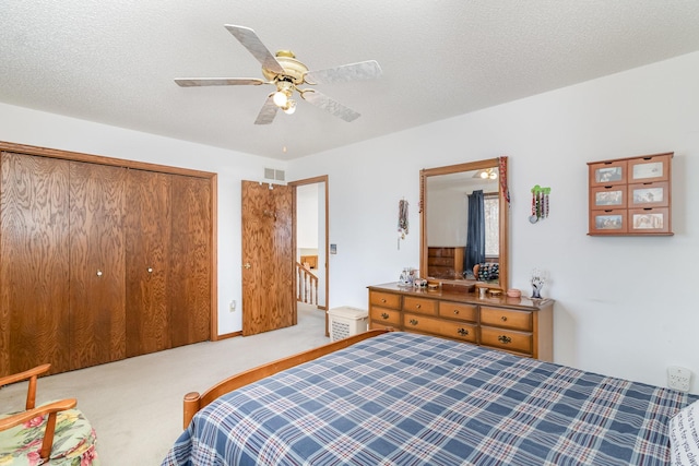 carpeted bedroom with a closet, visible vents, a textured ceiling, and a ceiling fan