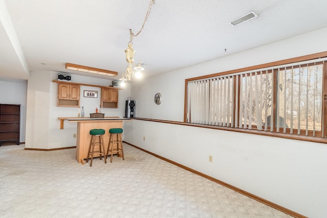 kitchen with baseboards, visible vents, light brown cabinetry, light carpet, and a kitchen breakfast bar