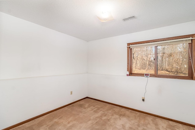 unfurnished room with a textured ceiling, light colored carpet, visible vents, and baseboards