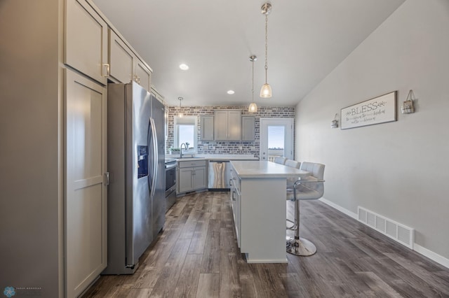 kitchen featuring a kitchen bar, visible vents, dark wood-type flooring, stainless steel appliances, and decorative backsplash