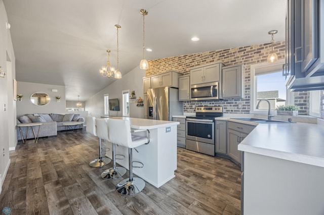 kitchen with gray cabinets, a sink, a kitchen breakfast bar, open floor plan, and stainless steel appliances