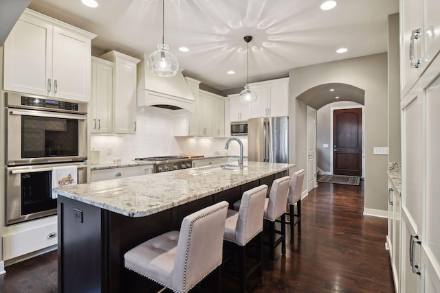 kitchen featuring backsplash, appliances with stainless steel finishes, arched walkways, white cabinetry, and a sink