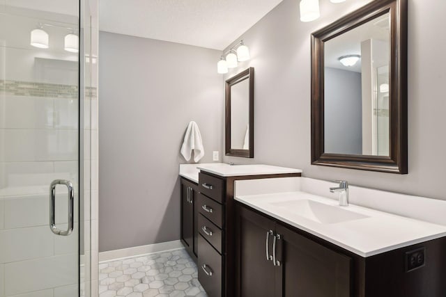 bathroom featuring baseboards, two vanities, a stall shower, a textured ceiling, and a sink