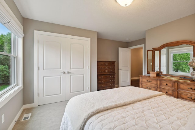 bedroom featuring a closet, visible vents, light colored carpet, and multiple windows