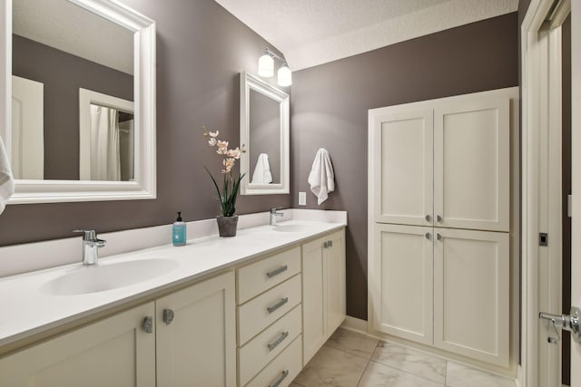 bathroom with a textured ceiling, double vanity, marble finish floor, and a sink