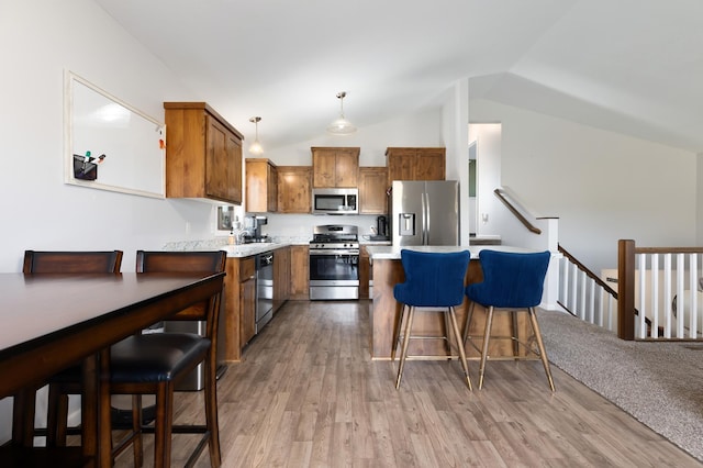 kitchen with brown cabinets, a breakfast bar, appliances with stainless steel finishes, light countertops, and lofted ceiling