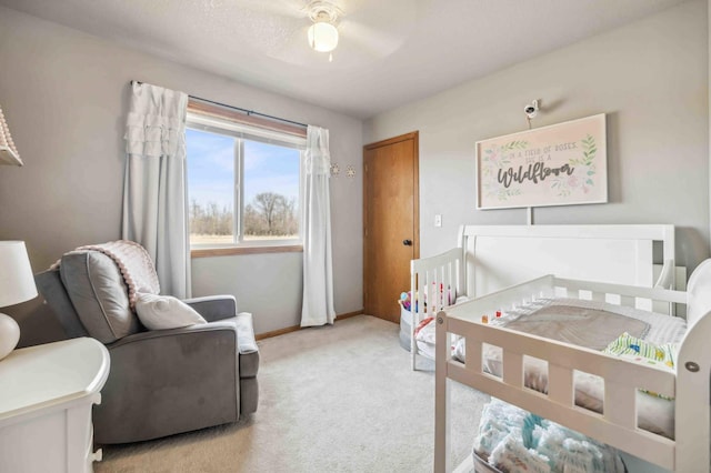 bedroom with a crib, light colored carpet, baseboards, and ceiling fan