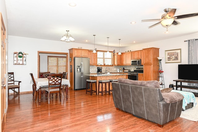 living room with recessed lighting, ceiling fan with notable chandelier, and light wood finished floors