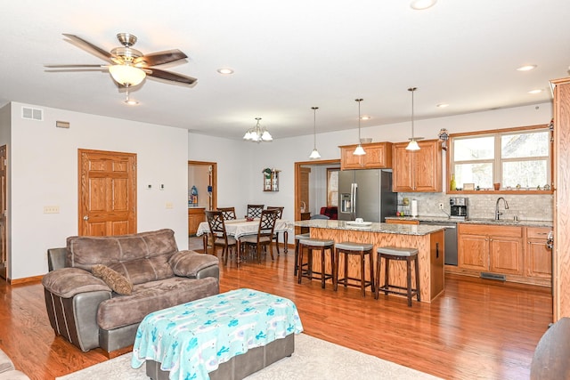 living area with recessed lighting, visible vents, wood finished floors, and ceiling fan with notable chandelier