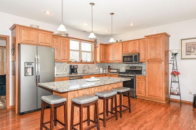 kitchen featuring decorative backsplash, appliances with stainless steel finishes, a kitchen island, and light wood-style floors