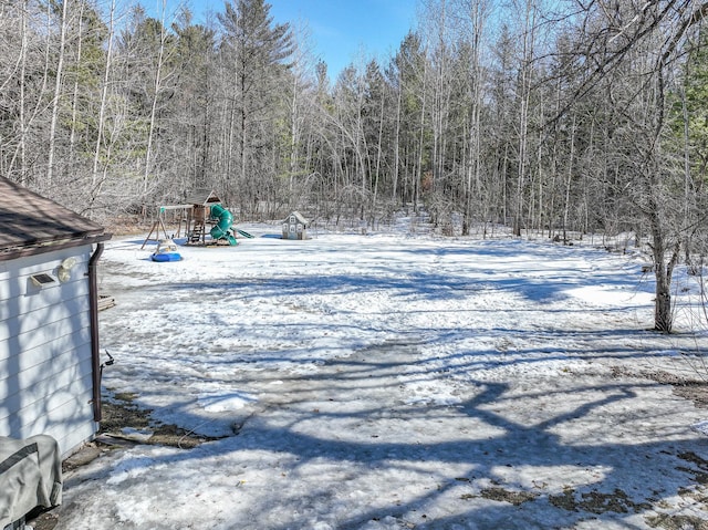 snowy yard featuring a playground and a wooded view