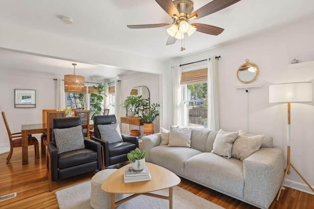 living area with visible vents, ceiling fan, baseboards, and wood finished floors