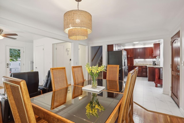 dining area with marble finish floor, ceiling fan with notable chandelier, and stairs