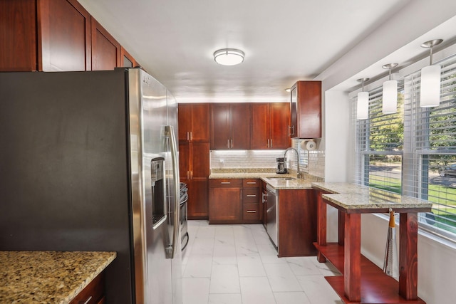 kitchen featuring a peninsula, a sink, stainless steel appliances, tasteful backsplash, and reddish brown cabinets