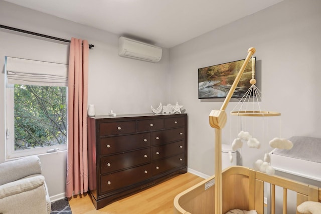 bedroom with a wall unit AC, baseboards, and light wood-type flooring