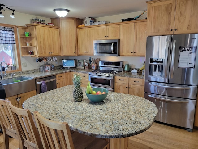 kitchen featuring light wood finished floors, a kitchen island, open shelves, a sink, and stainless steel appliances