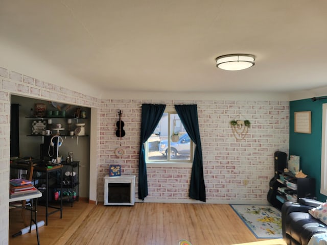 living area with brick wall and wood finished floors