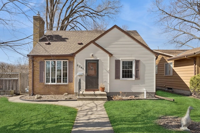 view of front of home featuring fence, roof with shingles, a front yard, brick siding, and a chimney