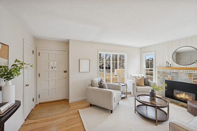 living room with a tiled fireplace, a textured ceiling, light wood-type flooring, and baseboards