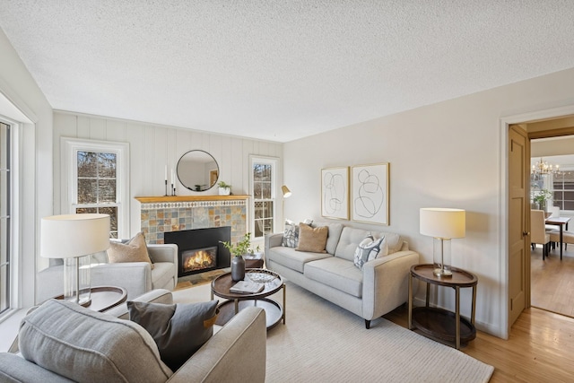 living room featuring a fireplace with flush hearth, a textured ceiling, an inviting chandelier, and wood finished floors