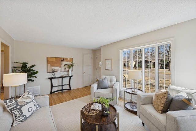 living area featuring visible vents, baseboards, a textured ceiling, and wood finished floors