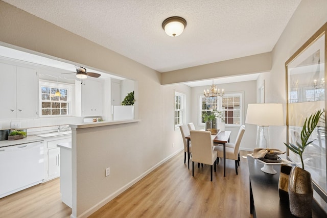 dining space featuring ceiling fan with notable chandelier, light wood-style flooring, a textured ceiling, and baseboards