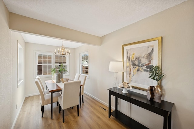 dining area with visible vents, baseboards, a textured ceiling, a notable chandelier, and light wood-type flooring