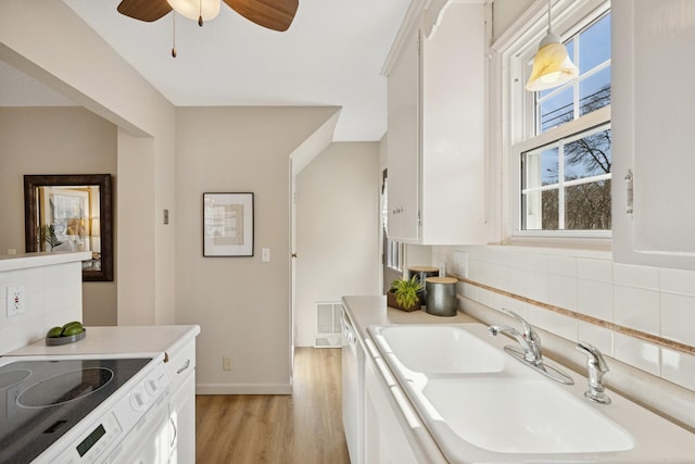 kitchen with backsplash, light countertops, light wood-style flooring, white cabinets, and a sink