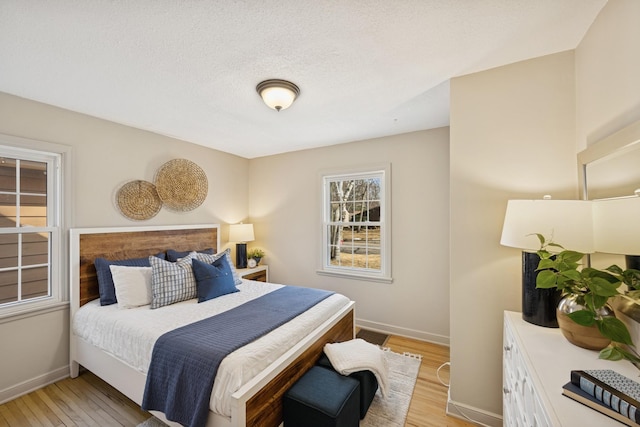 bedroom with light wood-type flooring, baseboards, and a textured ceiling