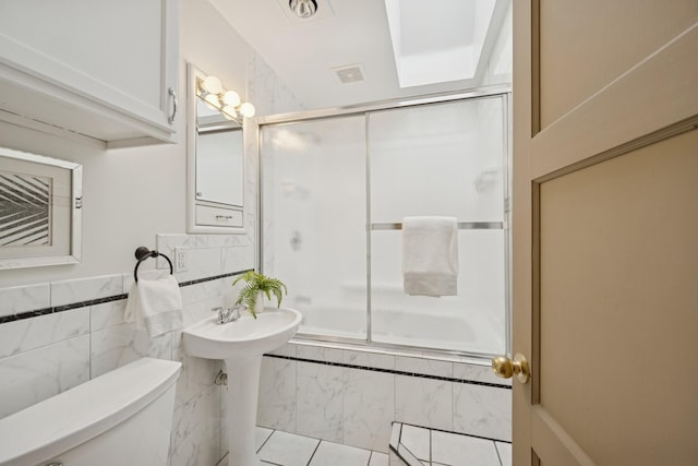 full bath with tiled shower / bath combo, toilet, and tile walls